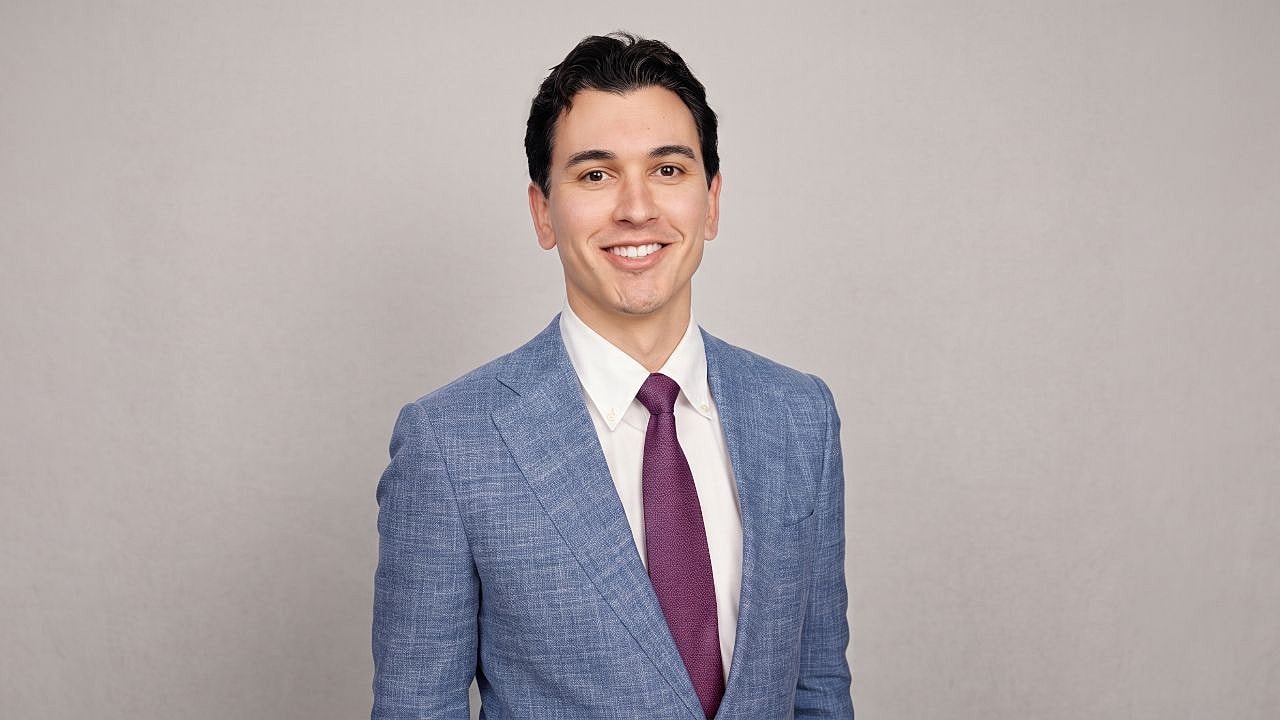 Smiling man in a blue suit against neutral background.