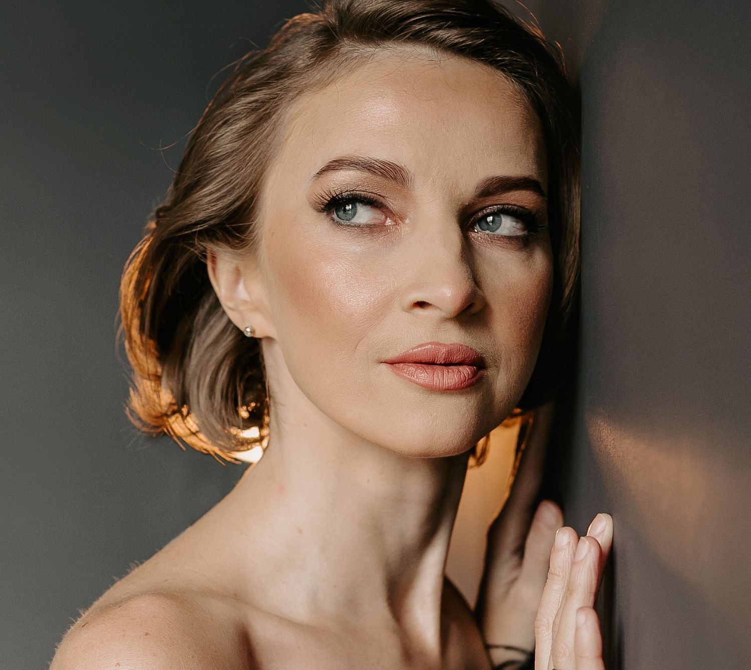 Woman with short hair posing against a wall.