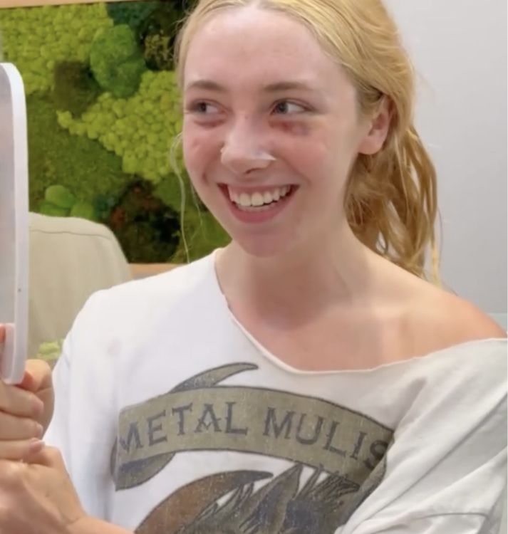 Smiling person holding a mirror, wearing a casual shirt.